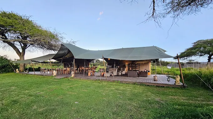 Luxury bush camp in Tanzania featuring a spacious safari tent with outdoor dining area and lush green surroundings